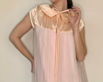 Op de afbeelding: Een lange, roze, doorschijnende nachtjapon met een satijnen bovenstuk en een strik aan de halslijn.