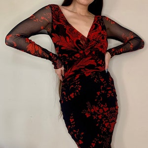 May include: A red and black floral print midi dress with long sheer sleeves. The dress has a V-neckline and a fitted silhouette.