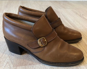 May include: A pair of brown leather ankle boots with a buckle fastening and a block heel.