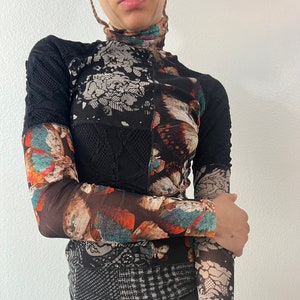 May include: A black long-sleeved shirt with a patchwork design featuring floral and butterfly patterns in shades of brown, orange, blue, and white.