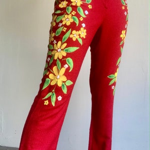 Op de afbeelding: Rode broek met geborduurd bloemmotief. De broek heeft gele bloemen, groene bladeren en kleine witte bloemen. Het bloemmotief staat op de voorkant van de broek. De broek heeft een rechte pijp.