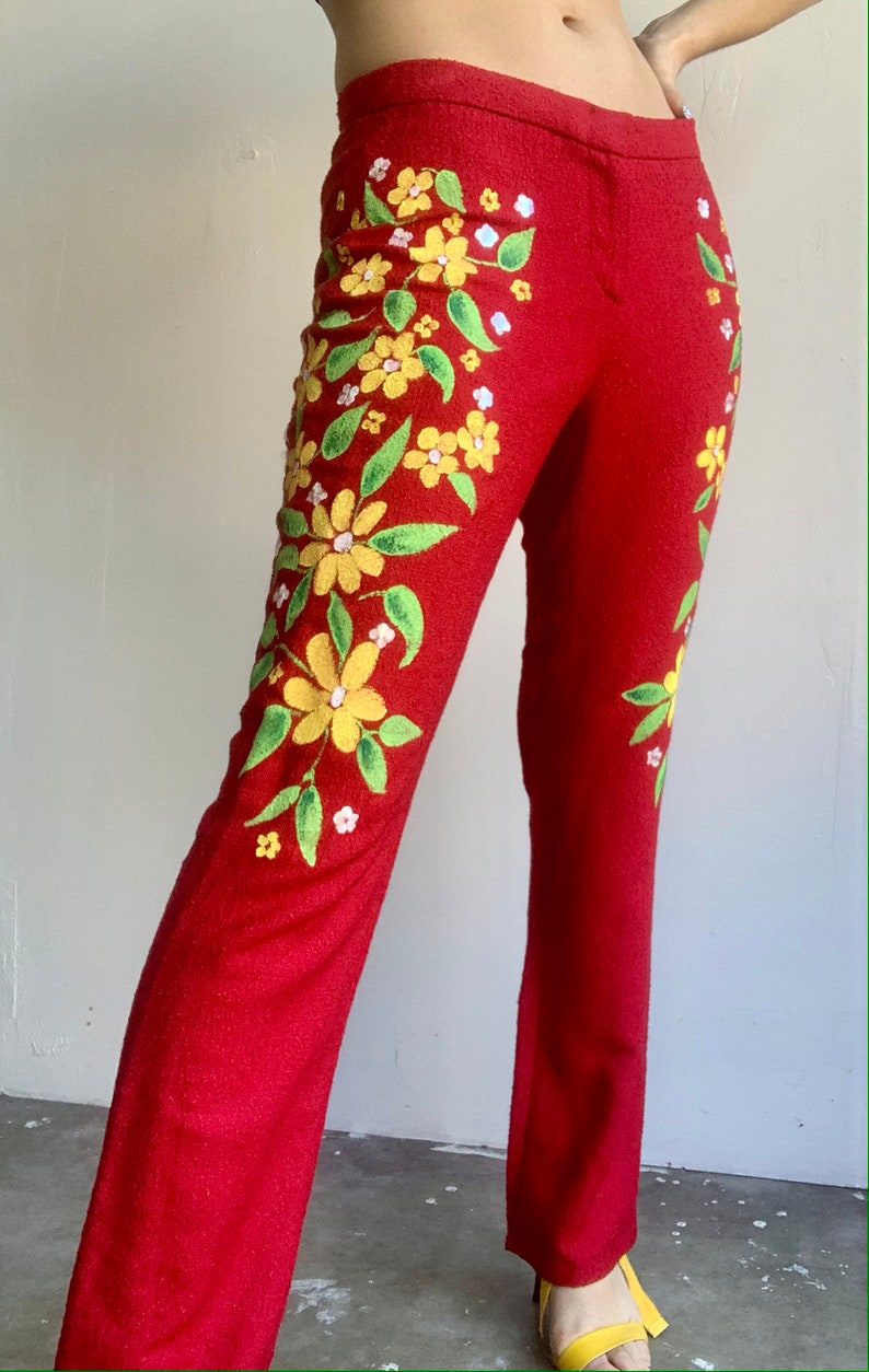 Op de afbeelding: Rode broek met geborduurd bloemmotief. De broek heeft gele bloemen, groene bladeren en kleine witte bloemen. Het bloemmotief staat op de voorkant van de broek. De broek heeft een rechte pijp.