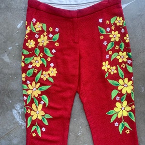 Op de afbeelding: Rode broek met een bloemenmotief. De broek heeft gele bloemen met groene bladeren en kleine witte bloemen. Het bloemenpatroon staat aan beide kanten. De broek heeft een rechte pijp.