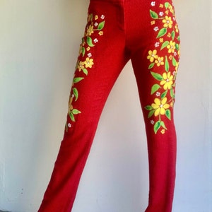 Op de afbeelding: Rode broek met bloemenpatroon. De broek is versierd met gele en witte bloemen en groene bladeren. De broek heeft een rechte pijp, een klassieke stijl.
