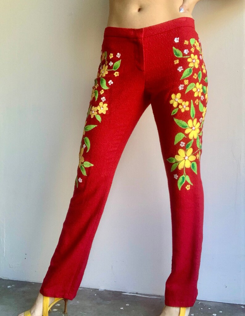 Op de afbeelding: Rode broek met bloemenpatroon. De broek is versierd met gele en witte bloemen en groene bladeren. De broek heeft een rechte pijp, een klassieke stijl.