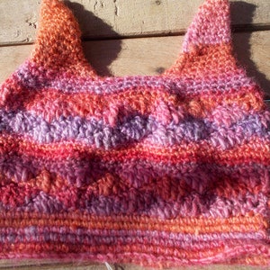 May include: A crocheted hat with a striped pattern in shades of pink, orange, and purple.