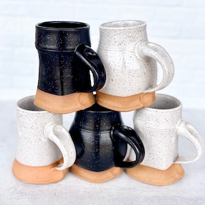 May include: Four ceramic mugs, two white with black speckles and two black with white speckles. The mugs have a brown rim and base.