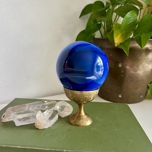 May include: A white ceramic mug with a black handle and the text "But First, Coffee" in a bold, black font. The mug is set against a blurred background, highlighting its clean design.