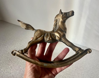 May include: A brass rocking horse figurine. The horse is in a galloping pose with its head turned to the side. The rocking base is made of brass and has a slightly aged patina.
