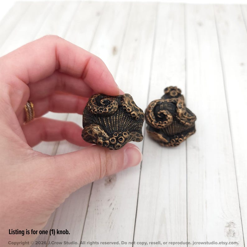May include: Two dark bronze-colored cabinet knobs featuring a sculpted octopus design with visible tentacles wrapped around a central shell-like texture. The knobs have a weathered, metallic finish with dark recessed areas and lighter highlights.