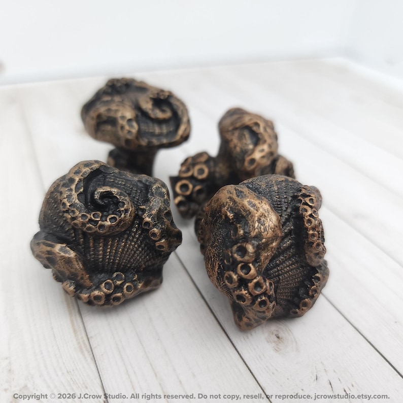 May include: Four cabinet knobs with a dark bronze finish, each featuring a detailed, three-dimensional octopus tentacle design wrapped around a textured shell-like base. The knobs have a weathered, metallic appearance with visible suction cups.