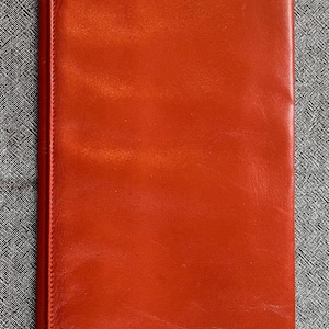 May include: A rectangular, red leather clutch with gold-colored corner accents. The clutch has a smooth, glossy finish and a simple, elegant design, suitable for formal occasions.