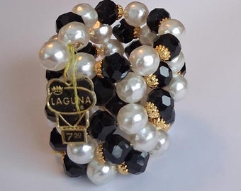May include: A beaded bracelet featuring a mix of white faux pearls and black faceted beads. The bracelet includes gold-colored accents and a gold-tone tag that reads "LAGUNA" and "7.50". The bracelet is a vintage style.
