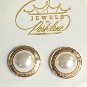 May include: A pair of gold-tone earrings with a white pearl center. The earrings are labeled "Jewels by Park Lane".