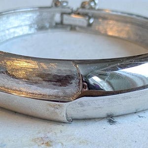 May include: A silver bangle bracelet with a textured finish and a hinged clasp.