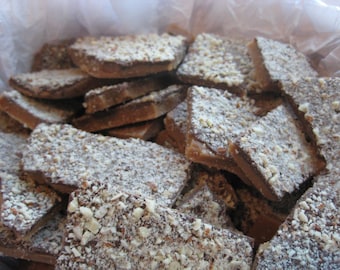 Puede incluir: Primer plano de una pila de caramelo de chocolate con almendras. El caramelo está roto en trozos irregulares y está cubierto con una capa de azúcar en polvo.