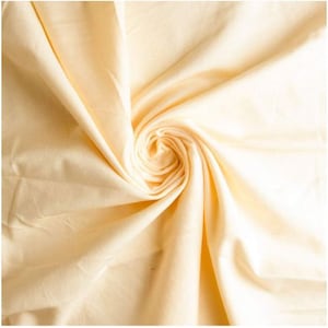 May include: A close-up of a soft, pale yellow fabric with a smooth texture. The fabric is folded and draped in a spiral pattern.