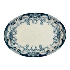May include: An oval ceramic platter featuring a cream-colored center and a wide, dark blue border. The border is decorated with intricate, symmetrical floral patterns in blue and white, accented with thin gold lines along the inner edge.