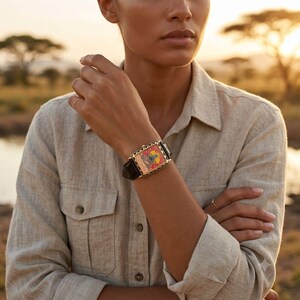 May include: A rectangular wristwatch with a black leather band and a gold-colored case. The watch face features a colorful illustration with red, yellow, and blue accents. The watch is worn on a wrist.