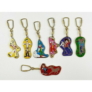 May include: Set of eight colorful metal keychains featuring different circus characters. Each keychain is shaped like a person and has a gold-colored ring.