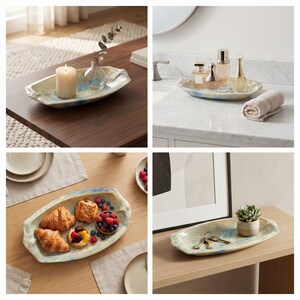 May include: An elongated, shallow ceramic tray with an irregular, organic shape and a glossy finish. The tray features a cream-colored base with subtle, blended streaks of light blue and tan throughout its surface, creating a marbled appearance.