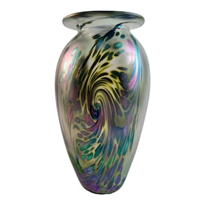 May include: A decorative glass vase with a wide body and a narrow neck. The vase features a swirling pattern of green, purple, and blue colours. The glass has an iridescent finish, giving it a shimmering appearance. The vase is suitable for displaying flowers or as a decorative accent.