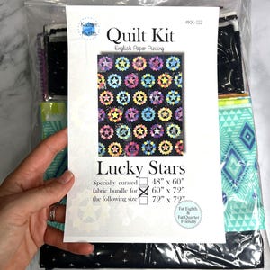 May include: A quilt kit in a clear plastic bag. The kit includes fabric and a pattern for a quilt with a star design. The pattern is labeled "Lucky Stars" and includes size options of 122cm x 152cm, 152cm x 183cm, and 183cm x 183cm.
