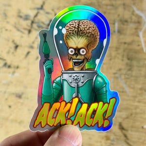 May include: Holographic sticker featuring a Martian character with a large brain, wearing a green space suit and holding a ray gun. The sticker has the text "ACK! ACK!" in a bold, colorful font. The design is vibrant and eye-catching.