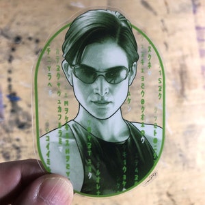 May include: A green and black sticker featuring a portrait of a person wearing sunglasses. The sticker has Japanese text around the border.