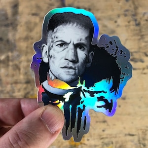 May include: A holographic sticker featuring a black and white portrait of a man with a serious expression. The background is black with a holographic effect.