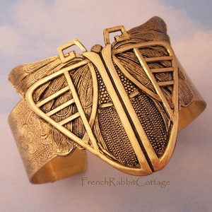 May include: A gold-toned metal cuff bracelet with a butterfly design. The butterfly wings are detailed with intricate patterns and the bracelet has a textured finish.