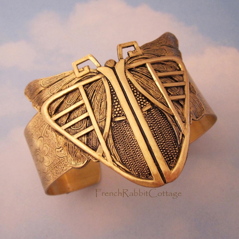 May include: A gold-toned metal cuff bracelet with a butterfly design. The butterfly wings are detailed with intricate patterns and the bracelet has a textured finish.