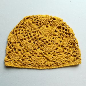 May include: A crocheted hat in a bright yellow color. The hat has a delicate, intricate pattern with a circular design.