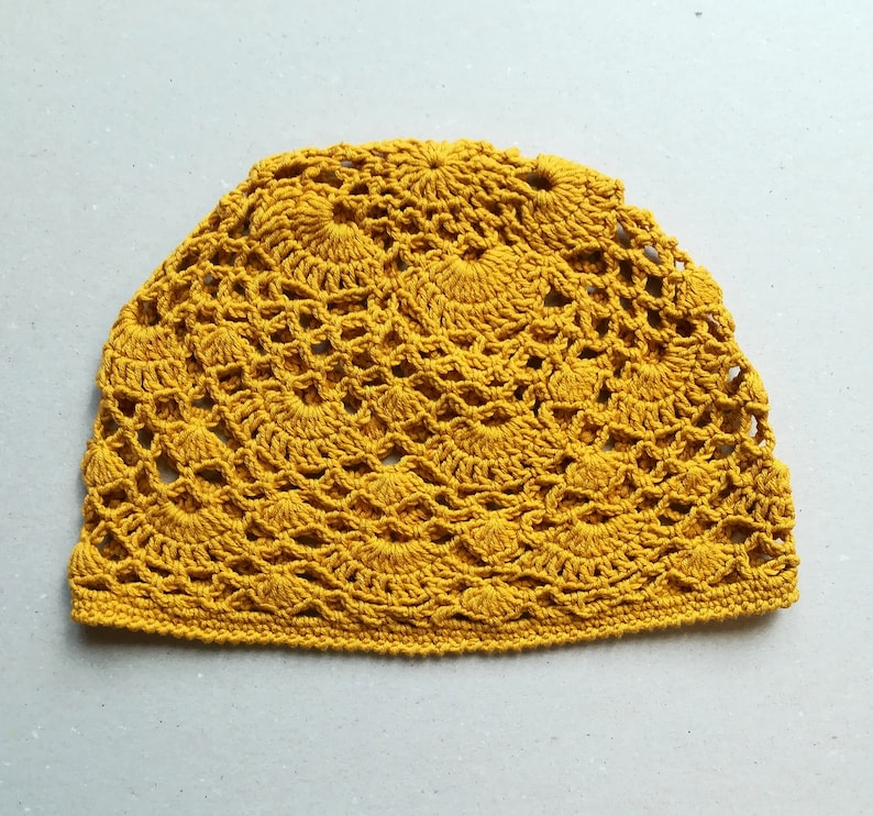 May include: A crocheted hat in a bright yellow color. The hat has a delicate, intricate pattern with a circular design.