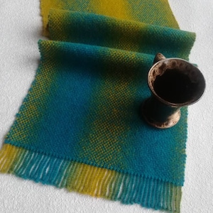 Op de afbeelding: Een geweven tafelloper met een blauw en geel ombre-patroon. De loper heeft franjes aan beide uiteinden en is gemaakt van een zacht, getextureerd garen.