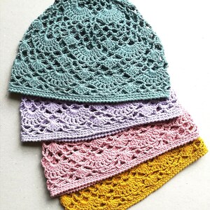 May include: Four crocheted hats in different colors: teal, lavender, pink, and yellow. The hats are stacked on top of each other, with the teal hat on top.