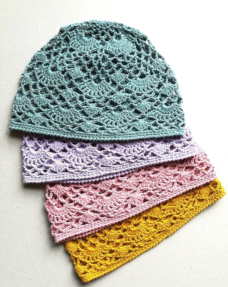 May include: Four crocheted hats in different colors: teal, lavender, pink, and yellow. The hats are stacked on top of each other, with the teal hat on top.