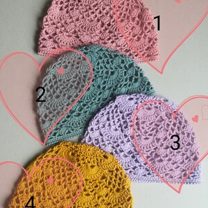 May include: Four crocheted hats in different colors: pink, green, purple, and yellow. The hats are arranged in a row, with the pink hat at the top and the yellow hat at the bottom.