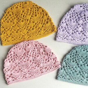 May include: Four crocheted hats in different colors: mustard yellow, light pink, lavender, and teal. The hats are made with a delicate, lacy stitch pattern.