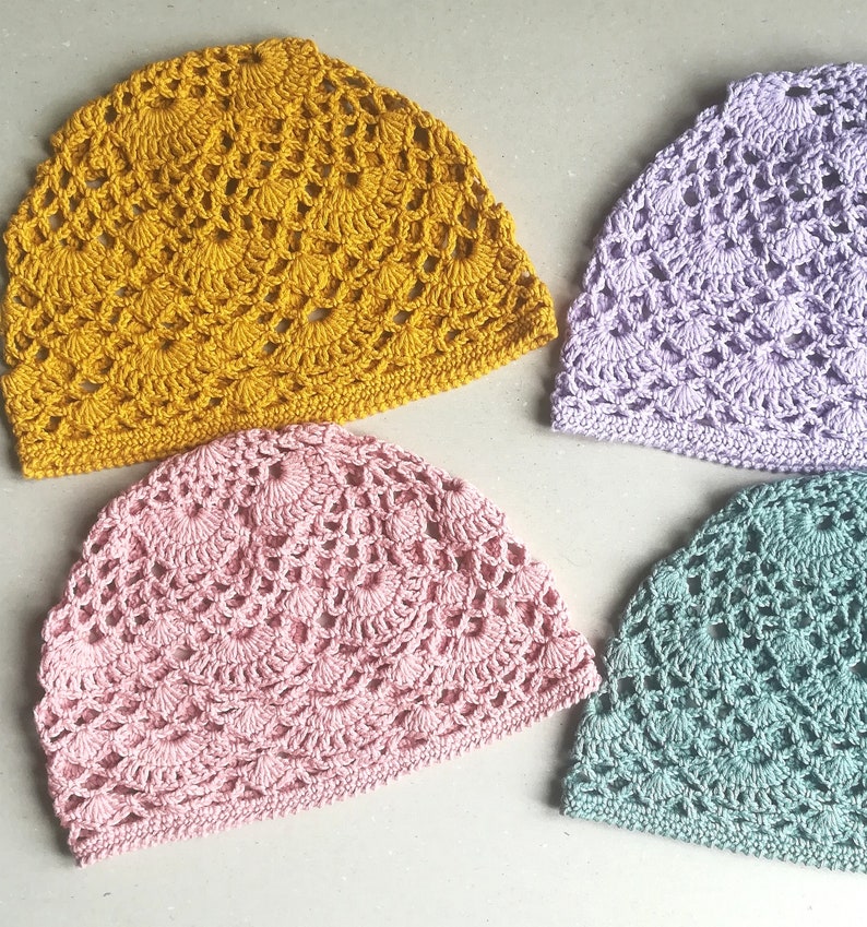 May include: Four crocheted hats in different colors: mustard yellow, light pink, lavender, and teal. The hats are made with a delicate, lacy stitch pattern.