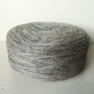 Puede incluir: Un ovillo de lana gris, enrollado en forma de bola.