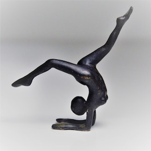 Puede incluir: Una escultura de metal negro de una persona en una postura de yoga. La persona está de pie sobre sus manos con las piernas en el aire.