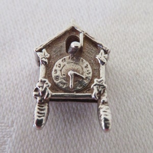 May include: A silver charm in the shape of a cuckoo clock. The clock face has Roman numerals and a single hand.