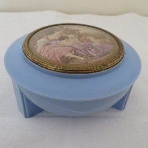 Può includere: Una scatola portaoggetti in plastica blu chiaro con un coperchio rotondo con bordo dorato che presenta un'illustrazione vintage di tre donne in un giardino.