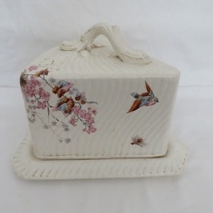 May include: White ceramic cheese dome with a handle and a matching base. The dome is decorated with a floral pattern and flying birds.