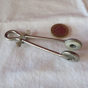 May include: Silver-toned metal tongs with white plastic tips. The tongs are about the size of a UK 20 pence coin.