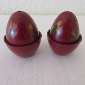 Puede incluir: Un juego de dos saleros y pimenteros rojos en forma de huevo con diseños florales amarillos y verdes.