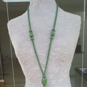 May include: A long green beaded necklace with a tassel at the end. The beads are oval shaped and the tassel is made of green yarn.
