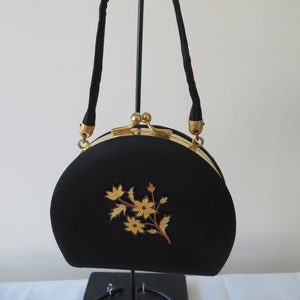 May include: A black satin evening bag with a gold clasp and floral embroidery. The bag has a short handle and a half-moon shape.
