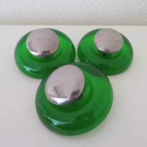 Può includere: Tre portacandele in vetro verde con cime argentate. I portacandele sono rotondi e hanno un bordo rialzato.